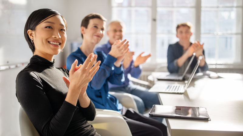 People clapping at a meeting with an Asian woman in the foreground

