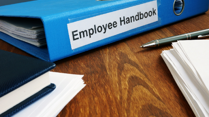 Employee Handbook manual in the folder, pen, and other documents on the table
