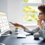 Project manager checking and updating tasks and milestones progress planning with scheduling interface on a desktop computer with two screens