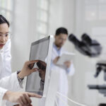 A Caucasian male and Asian female scientist dressed in lab coats looking at a computer screen