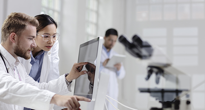 A Caucasian male and Asian female scientist dressed in lab coats looking at a computer screen