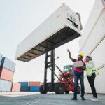 Black foreman and a woman worker checking a container cargo harbor holding laptop and using walkie talkie
