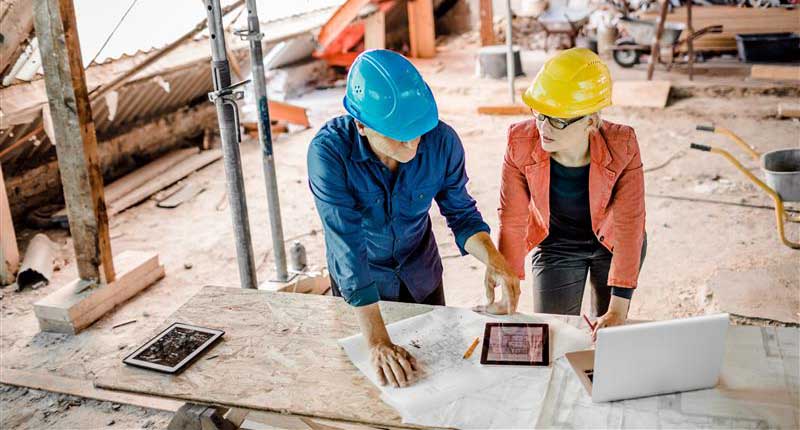 An architect and a worker working together at a construction site, wearing safety gear