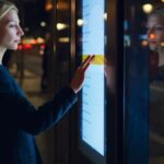 A female standing near a big touchscreen display, scrolling to check information