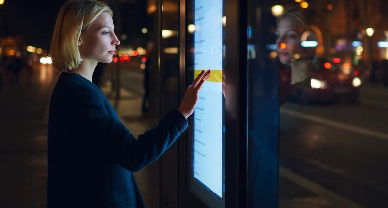 A female standing near a big touchscreen display, scrolling to check information